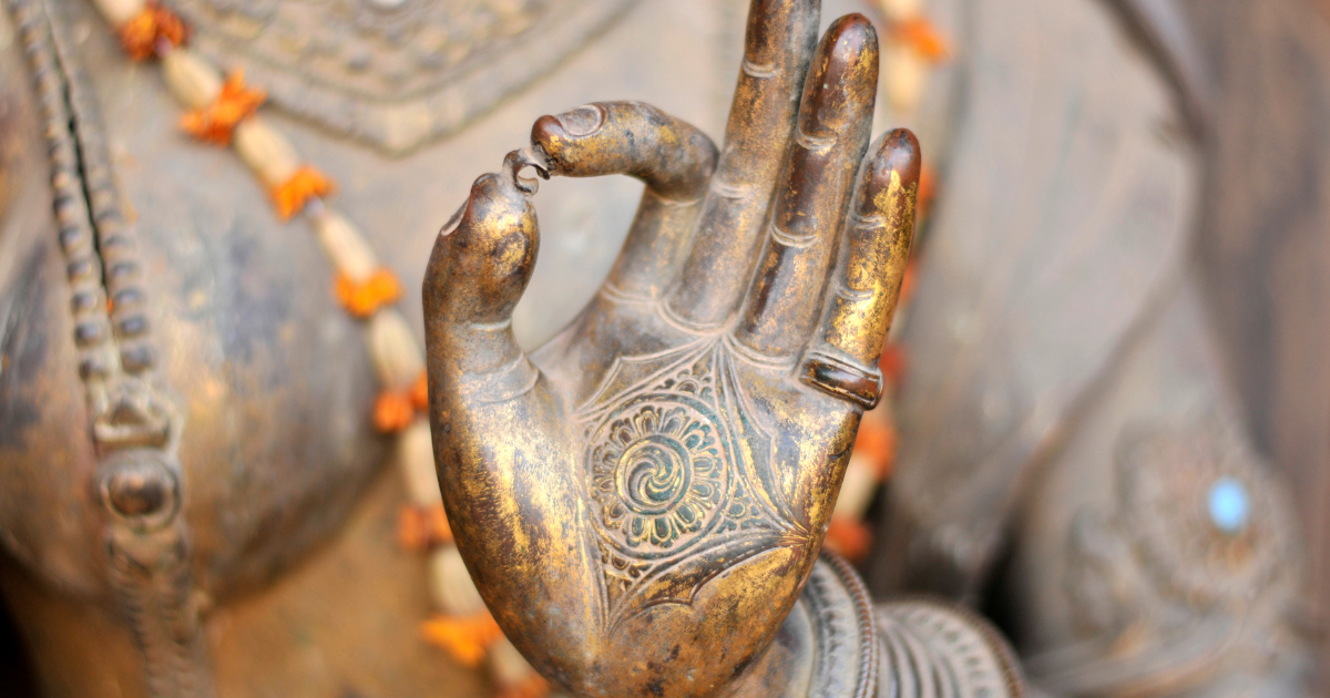 Main d’une statue en métal effectuant un mudrā, montrant des motifs gravés au centre de la paume.